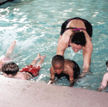 Instructor assists toddler in kicking in the water as part of a swim lesson.